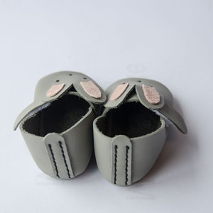 May include: A pair of gray leather baby shoes with pink bunny ears.