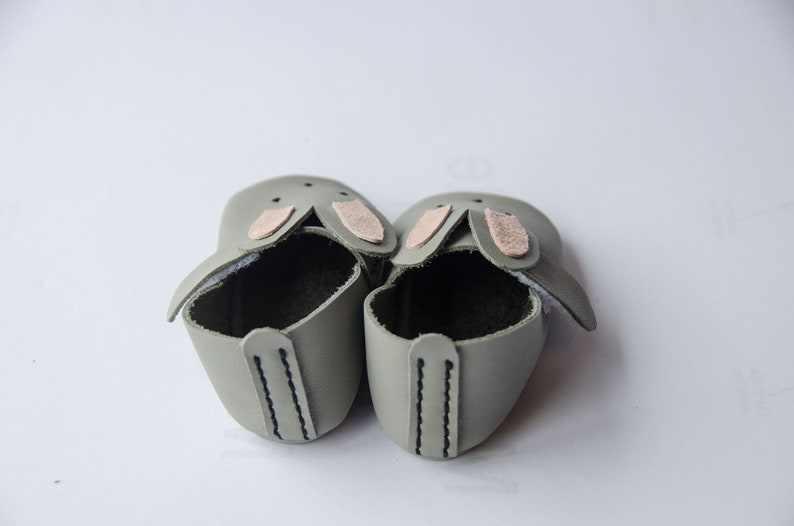 May include: A pair of gray leather baby shoes with pink bunny ears.