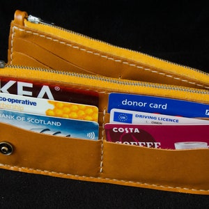 May include: A yellow leather wallet with a zipper closure. The wallet is open and contains several cards, including an IKEA membership card, a Bank of Scotland card, a donor card, a driving license, and a Costa Coffee card.