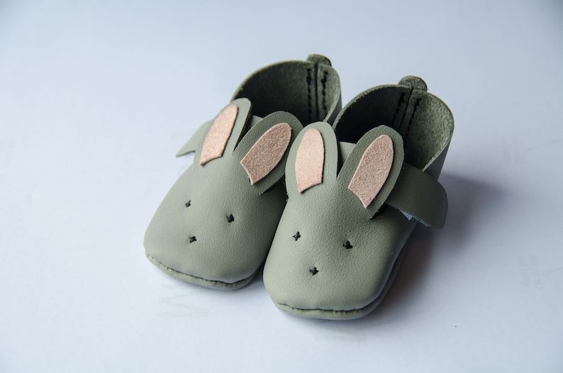 May include: A pair of green leather baby shoes with pink felt bunny ears.