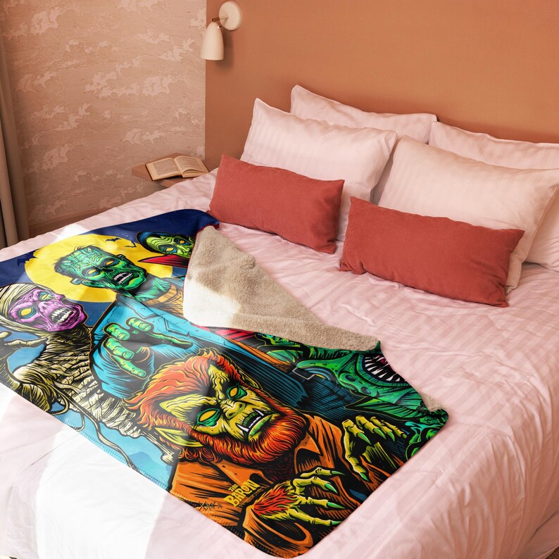 Puede incluir: Una manta de forro polar colorida con un estampado gr&aacute;fico de varios monstruos, incluyendo un hombre lobo, una momia y un monstruo de Frankenstein. La manta est&aacute; sobre una cama con almohadas.