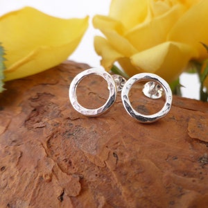May include: A pair of silver hammered circle stud earrings. The earrings are small and delicate, and they have a simple, modern design.
