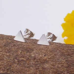 May include: A pair of silver triangle stud earrings. The earrings are small and simple, and they are perfect for everyday wear.