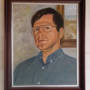 May include: A framed oil painting of a man wearing glasses and a blue shirt. The painting is signed "S. Laivama-O."