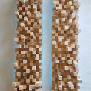 May include: Two wooden acoustic panels with a light brown finish. Each panel is made up of small, square blocks arranged in a random pattern. The panels are mounted on a white wall and are connected to black cords with black plugs.