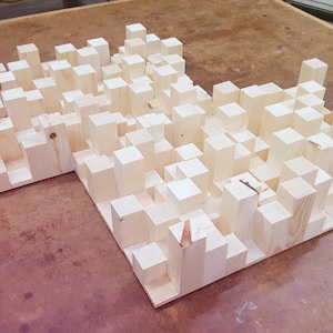 以下が含まれることがあります： 多くの小さな長方形の木材のブロックでできた木製のサウンドパネル。ブロックはランダムなパターンで配置されており、テクスチャのある表面を作り出しています。パネルは薄い茶色で、未完成のようです。