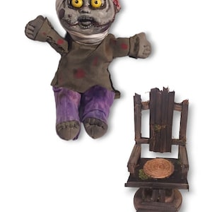May include: A handmade plush zombie doll with a bandage on its head, wearing a green shirt and purple pants, sitting in front of a wooden chair with a woven seat.