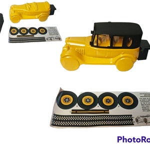 May include: A yellow toy car with a black roof and a black boot. The car has four wheels and is missing one of its wheels. The car is on a white background. The car is a vintage style car.