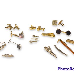 May include: A collection of gold-toned cufflinks, tie clips, and a key-shaped pin. The cufflinks feature various designs, including a square with an initial, a pair with a mother-of-pearl inlay, and a pair with a geometric design. The tie clips are in various shapes, including a straight bar, a curved bar, and a key shape. The key-shaped pin has a detailed design and a gold-toned finish.