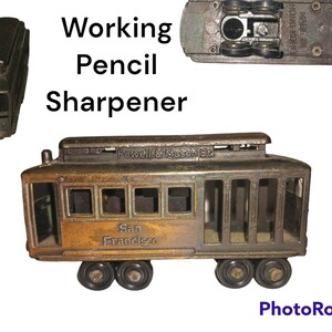 May include: A vintage metal pencil sharpener shaped like a San Francisco cable car. The sharpener is brown and has the words "Powell & Mason St." and "San Francisco" on the side. It has a working pencil sharpener mechanism.