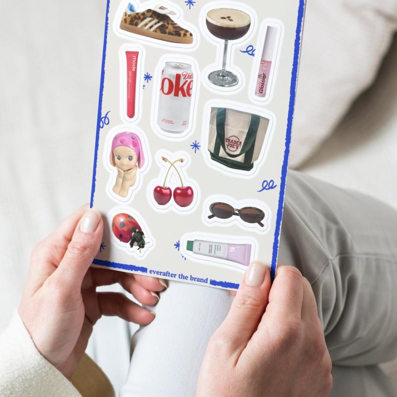 May include: A sheet of stickers with various designs, including a pair of cherries, a ladybug, a doll, a can of soda, a pair of sunglasses, a small bag, a tube of lip balm, and a glass of cocktail. The stickers are on a white background with blue accents.