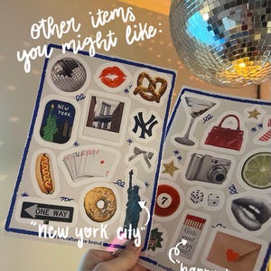 Pu&ograve; includere: Due fogli di adesivi con varie illustrazioni. Un foglio presenta una palla da discoteca, labbra, un pretzel e monumenti di New York. L'altro include un bicchiere da Martini, una fotocamera e dadi. Il testo sui fogli recita "new york city" e "happy hour".