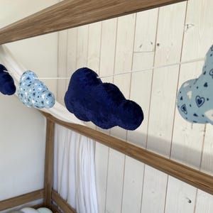 Può includere: Una ghirlanda di decorazioni a forma di nuvola in peluche nei toni del blu. Alcune nuvole sono blu navy, mentre altre sono azzurre con un motivo a cuore. La ghirlanda è infilata su un cordoncino bianco, adatta per l'arredamento della cameretta.