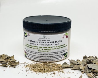 May include: A white jar with a black lid labeled "Protein Deep Hair Mask Strength & Moisture Balance" with a list of ingredients. The jar is sitting on a white surface with dried leaves scattered around it.