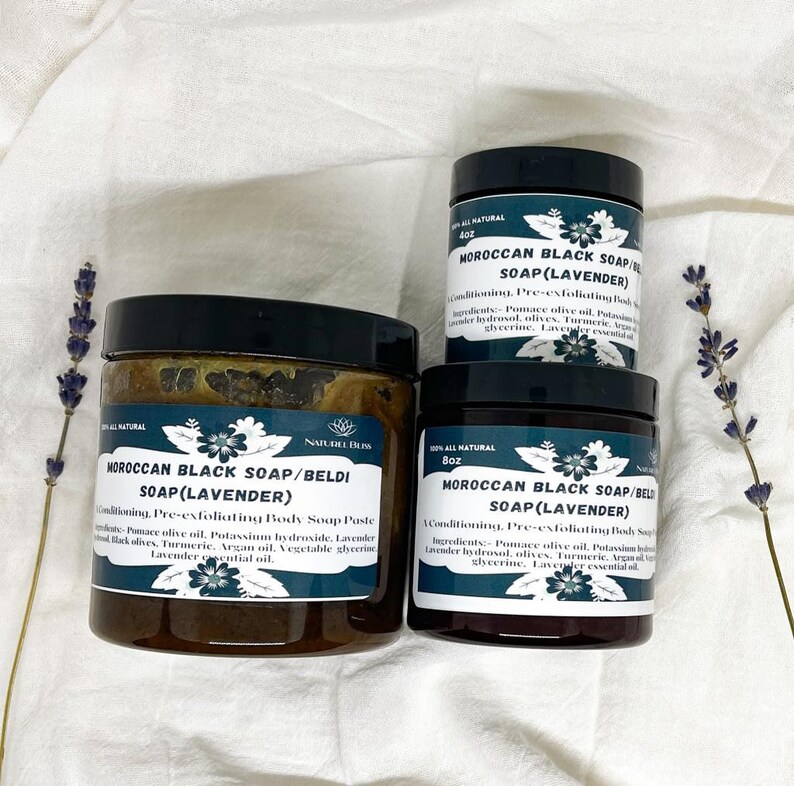 K&ouml;nnte beinhalten: Drei Gl&auml;ser mit marokkanischer schwarzer Seife mit Lavendel-&Ouml;l. Die Gl&auml;ser sind mit "Marokkanische schwarze Seife/Beldi Seife (Lavendel)" beschriftet und haben ein Fassungsverm&ouml;gen von 4 oz, 8 oz und 8 oz. Die Gl&auml;ser stehen auf einem wei&szlig;en Stoffuntergrund mit Lavendelbl&uuml;ten.