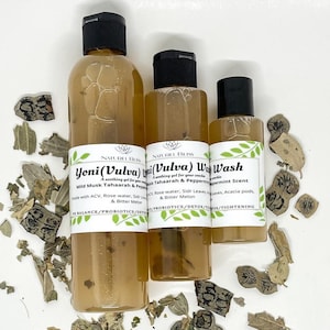 May include: Three clear glass bottles with brown liquid and black caps. The bottles are labeled "Yoni (Vulva) Wash", "Vulva Wash", and "Wash". The labels also include information about the ingredients and benefits of the products. The bottles are sitting on a white surface with dried leaves scattered around them.