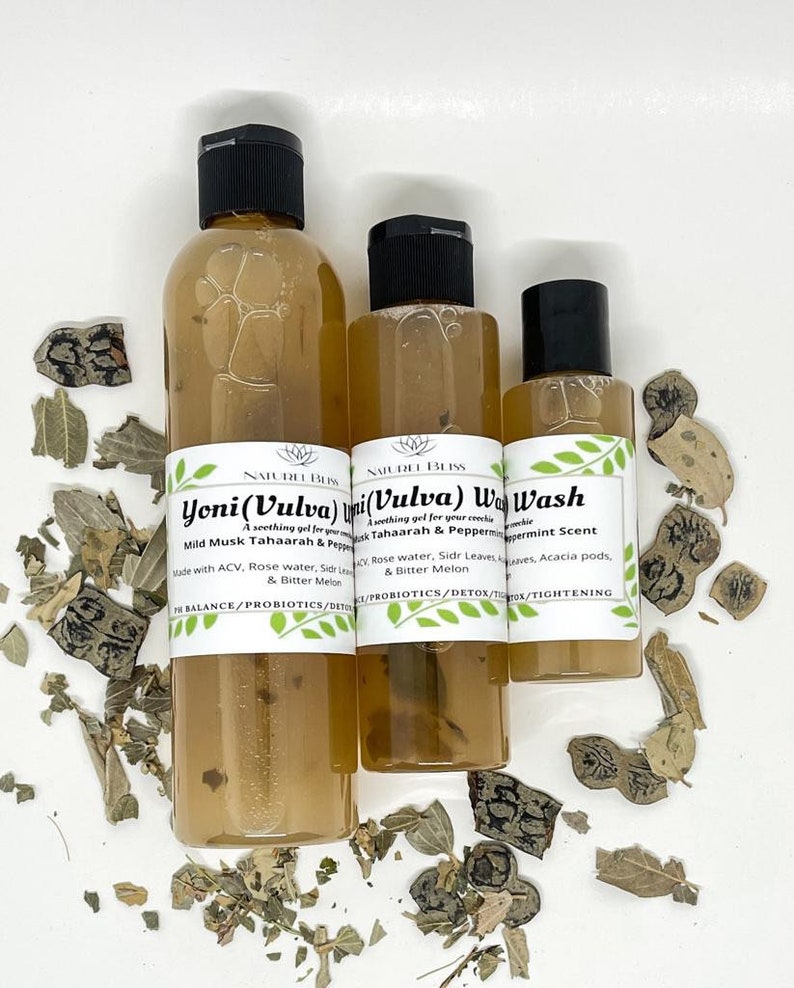 May include: Three clear glass bottles with brown liquid and black caps. The bottles are labeled "Yoni (Vulva) Wash", "Vulva Wash", and "Wash". The labels also include information about the ingredients and benefits of the products. The bottles are sitting on a white surface with dried leaves scattered around them.