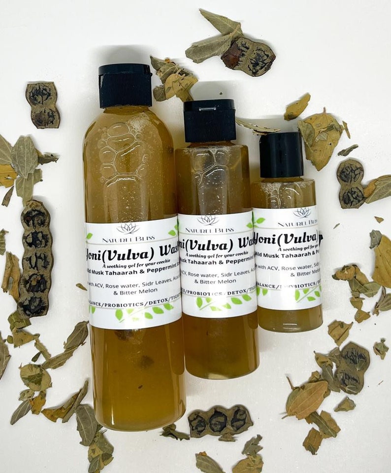 May include: Three amber glass bottles with black caps and labels that read "Joni (Vulva) Wash", "Yoni (Vulva) Wash", and "Yoni (Vulva) Wash". The bottles are on a white surface with dried leaves scattered around them.