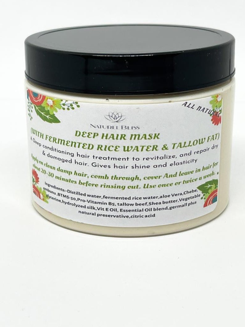 May include: A white jar with a black lid labeled "Deep Hair Mask with Fermented Rice Water & Tallow Fat". The jar is filled with a light beige cream and has a floral design on the front. The label also includes the text "Naturel Bliss" and "All Natural".