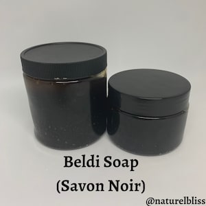 K&ouml;nnte beinhalten: Zwei schwarze Gl&auml;ser mit Beldi-Seife (Savon Noir) und schwarzen Deckeln. Die Gl&auml;ser sind unterschiedlich gro&szlig;. Der Text "Beldi Soap (Savon Noir)" und "@naturelbliss" ist auf wei&szlig;em Hintergrund unter den Gl&auml;sern gedruckt.