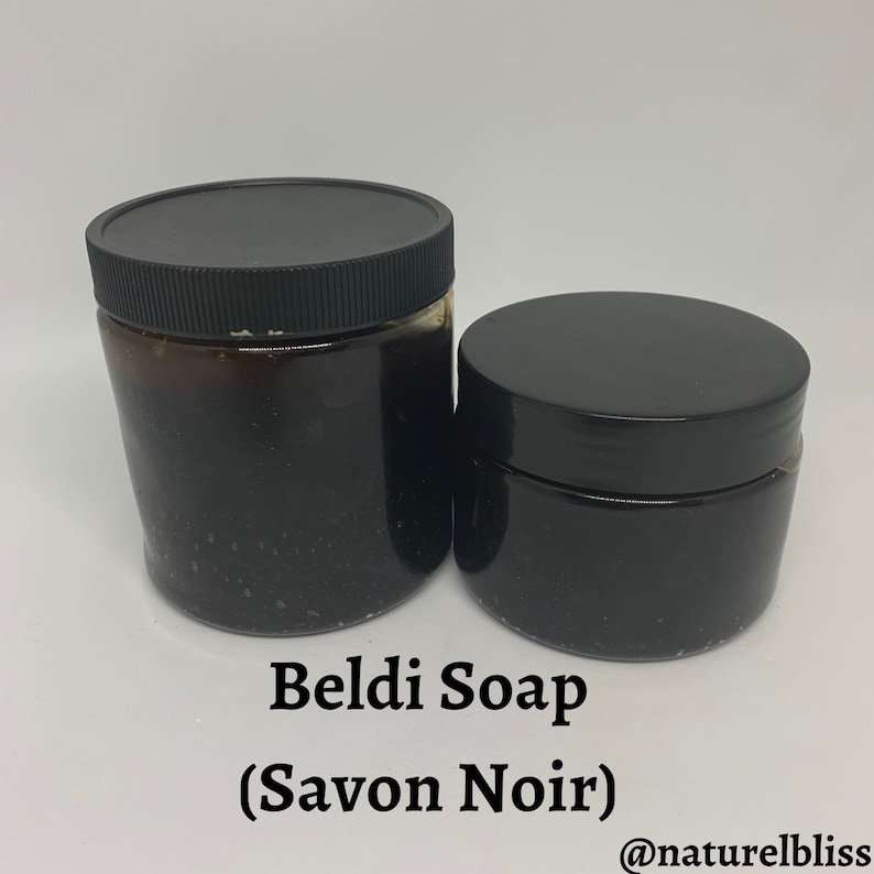 K&ouml;nnte beinhalten: Zwei schwarze Gl&auml;ser mit Beldi-Seife (Savon Noir) und schwarzen Deckeln. Die Gl&auml;ser sind unterschiedlich gro&szlig;. Der Text "Beldi Soap (Savon Noir)" und "@naturelbliss" ist auf wei&szlig;em Hintergrund unter den Gl&auml;sern gedruckt.