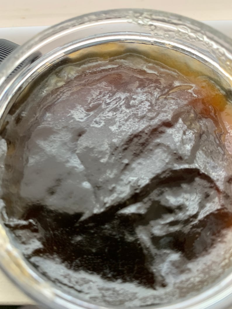 K&ouml;nnte beinhalten: Nahaufnahme eines Glasbeh&auml;lters, gef&uuml;llt mit einer dunkelbraunen Fl&uuml;ssigkeit. Die Fl&uuml;ssigkeit hat eine dicke, viskose Konsistenz und eine wei&szlig;e, schaumige Schicht obenauf.