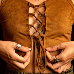 Puede incluir: Un top corto de ante marrón con un frente de encaje y un cierre de corbata. El top se usa sobre una camisa verde.