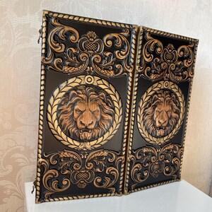 Op de afbeelding: Twee zwarte houten panelen met gouden randen en sierlijke houtsnijwerk. Elk paneel heeft een gouden leeuwenkop in een krans.