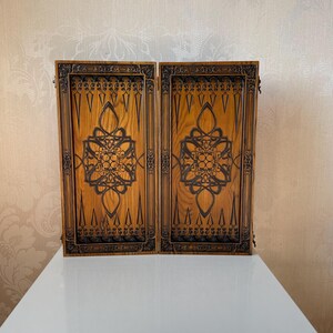 Op de afbeelding: Twee houten panelen met ingewikkelde gesneden ontwerpen. De panelen zijn bruin met donkerbruine snijwerk. De snijwerk is geometrisch en symmetrisch.