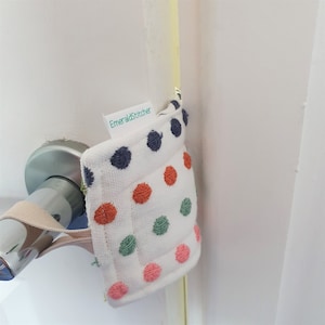 May include: A white doorstop with a polka dot pattern in shades of blue, orange, green, and pink. The doorstop has a loop for hanging and a label that reads "EmeraldStitcher".