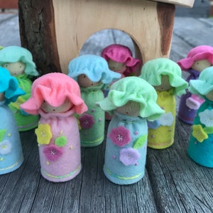 Puede incluir: Un conjunto de ocho muñecas de fieltro con flores bordadas y sombreros con volantes en colores pastel, incluyendo rosa, azul, verde y amarillo.