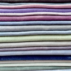 May include: A stack of 18 fabric squares in various shades of blue, green, purple, and gray. The fabric is soft and has a slightly textured surface.
