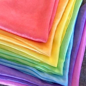 May include: A set of rainbow-colored silk scarves, folded in a triangle shape, with the colors ranging from pink to purple.