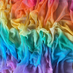 May include: A colourful, flowing fabric in a rainbow of hues, shifting from pink to orange, yellow, green, blue, and purple. The sheer material is draped and gathered, creating soft folds and a textured appearance.