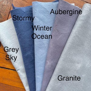 May include: Five fabric swatches in different shades of blue and gray. The swatches are labeled "Grey Sky", "Stormy", "Winter Ocean", "Aubergine", and "Granite".
