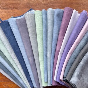 May include: A collection of 20 fabric swatches in various shades of blue, gray, and purple. The swatches are arranged in a fan shape, with the darkest shades at the bottom and the lightest shades at the top.