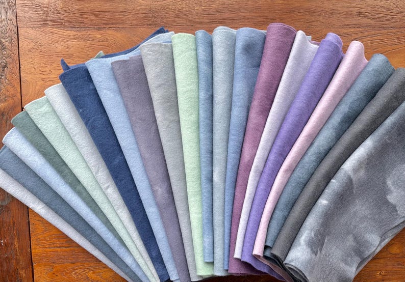 May include: A collection of 20 fabric swatches in various shades of blue, gray, and purple. The swatches are arranged in a fan shape, with the darkest shades at the bottom and the lightest shades at the top.