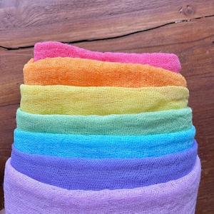 May include: A stack of rainbow coloured gauze fabric squares. The fabric is soft and sheer, and the colours are vibrant. The fabric is arranged in a rainbow order, with the top layer being pink and the bottom layer being purple.