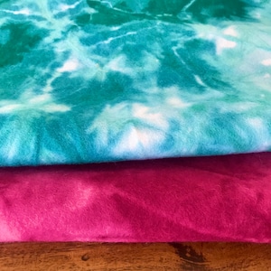 May include: Two pieces of fabric folded on top of each other. The top piece is a teal blue and white tie-dye pattern. The bottom piece is a deep pink and white tie-dye pattern.