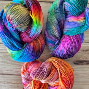 May include: Three skeins of colourful yarn in shades of blue, green, purple, orange, pink, and yellow. The yarn is arranged in a circular shape.