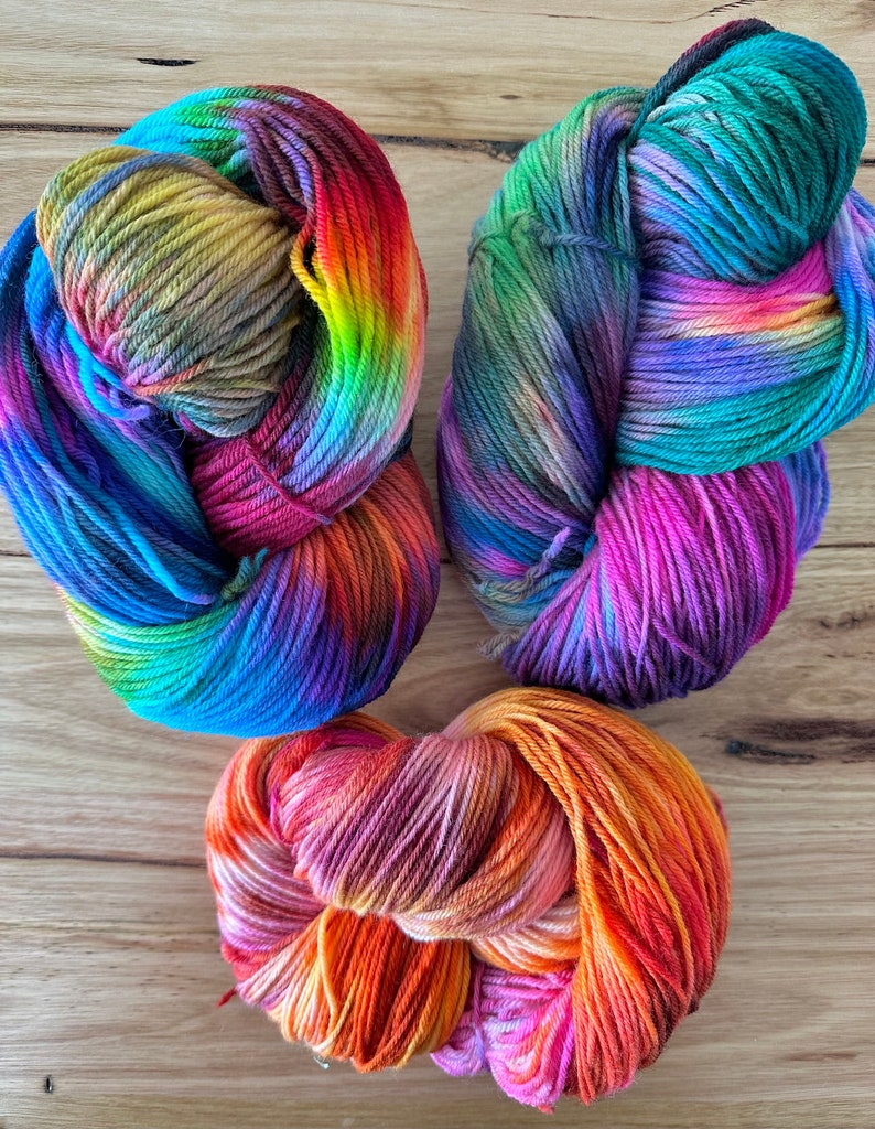 May include: Three skeins of colourful yarn in shades of blue, green, purple, orange, pink, and yellow. The yarn is arranged in a circular shape.