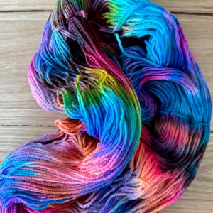 May include: A skein of colourful yarn with shades of blue, green, purple, orange, and pink. The yarn is hand-dyed and has a variegated colour pattern.