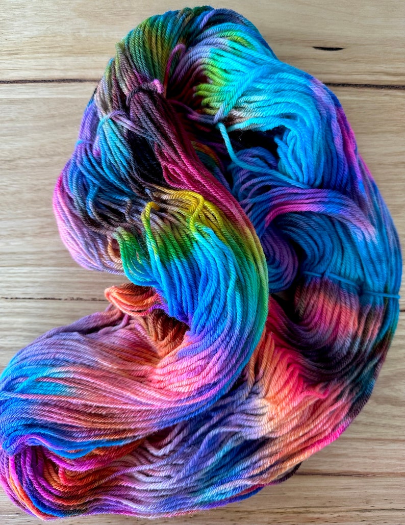 May include: A skein of colourful yarn with shades of blue, green, purple, orange, and pink. The yarn is hand-dyed and has a variegated colour pattern.