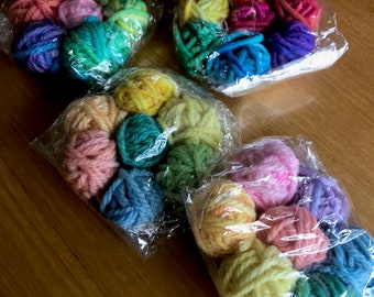 May include: Assortment of colorful yarn balls in plastic bags. The yarn is in shades of pink, blue, green, yellow, and purple.