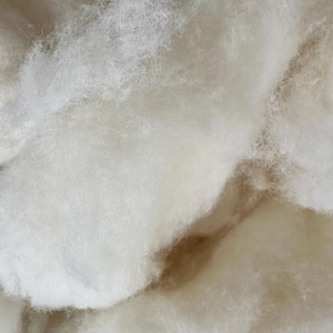 May include: A mass of white polyester fibre-fill stuffing with a soft, airy, and cloud-like texture. The material consists of fine, intertwined synthetic strands that create a voluminous, fluffy appearance with varying density throughout the cluster.