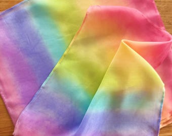 May include: A rainbow-colored silk scarf with a gradient of purple, blue, green, yellow, orange, and pink. The scarf is folded in half and the edges are sewn.
