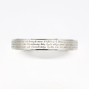 Könnte beinhalten: Ein silberfarbenes Armband mit eingraviertem griechischem Text. Das Armband hat ein schlichtes Banddesign, wobei der Text den gesamten Umfang umschließt. Der Text ist in einer klassischen Schriftart und gleichmäßig um das Band angeordnet.