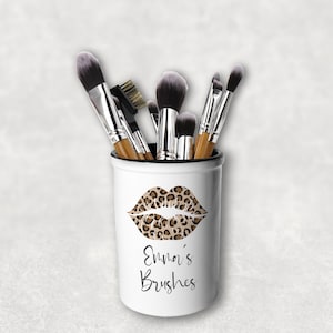 Könnte beinhalten: Weißer Keramik-Make-up-Pinselhalter mit einem Leoparden-Lippenmuster. Der Text "Emnor's Brushes" ist auf den Halter gedruckt. Der Halter ist mit verschiedenen Make-up-Pinseln gefüllt.