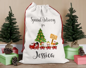 May include: A white Christmas gift bag with a red drawstring, featuring a festive design. The bag is printed with the words "Special Delivery for Jessica", a Christmas tree, and a train carrying snowmen. The bag is surrounded by small Christmas trees and gifts.