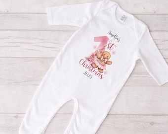 May include: White baby onesie with long sleeves. The onesie features a pink number 1, a Christmas tree, and a gingerbread person graphic. Text on the onesie reads "Amelia's 1st Christmas 2025".